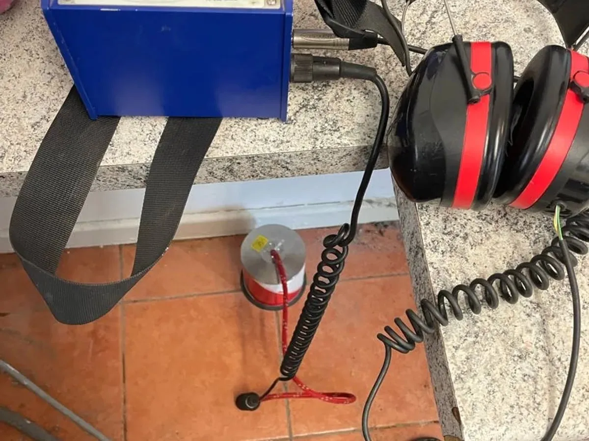 Blue acoustic amplifier and ear defenders on a kitchen worktop, with a red and white ground microphone on the terracotta floor tiles below