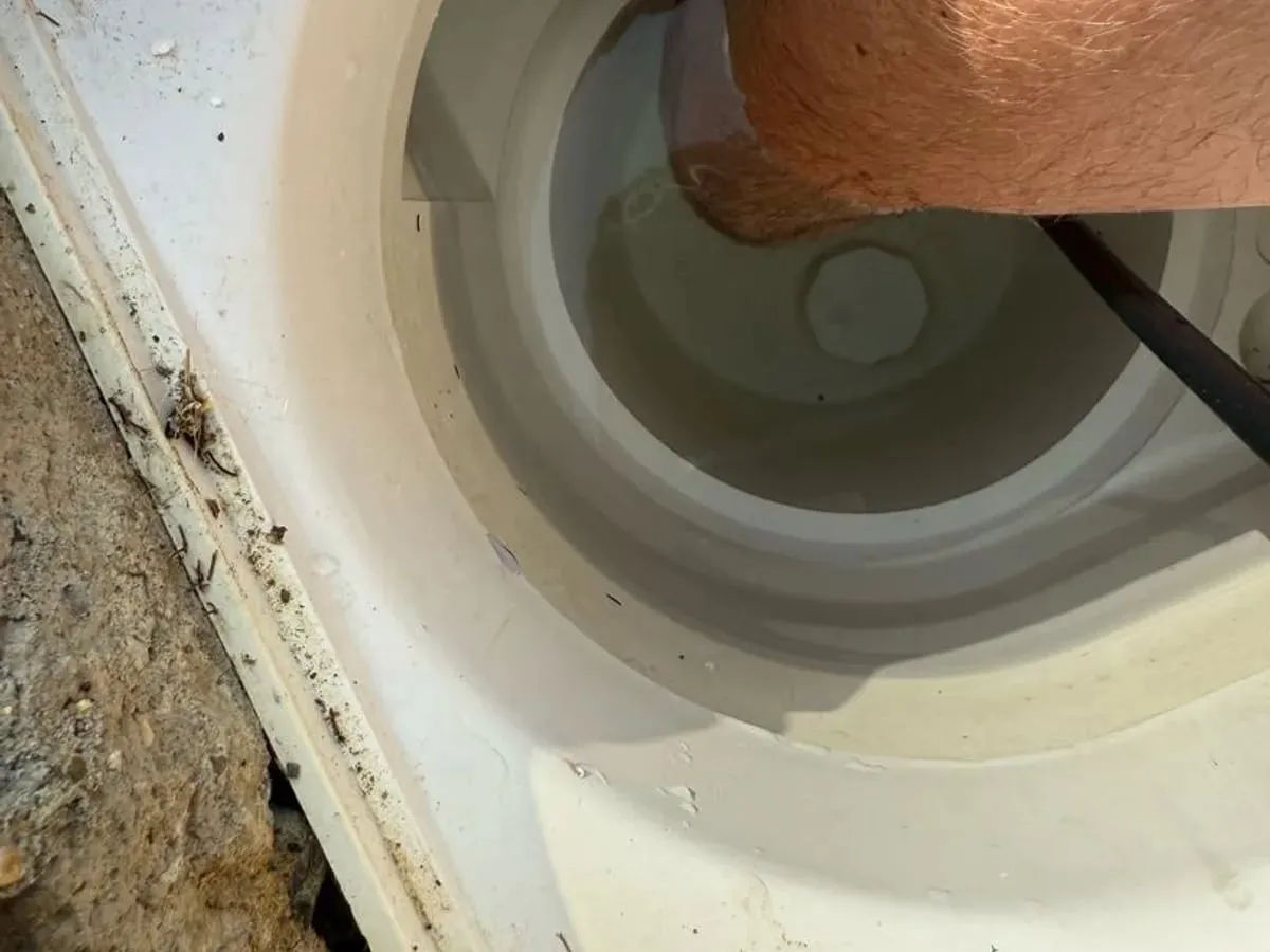 An engineer lowers the black lead of a hydrophone into the water in a white pool skimmer pot