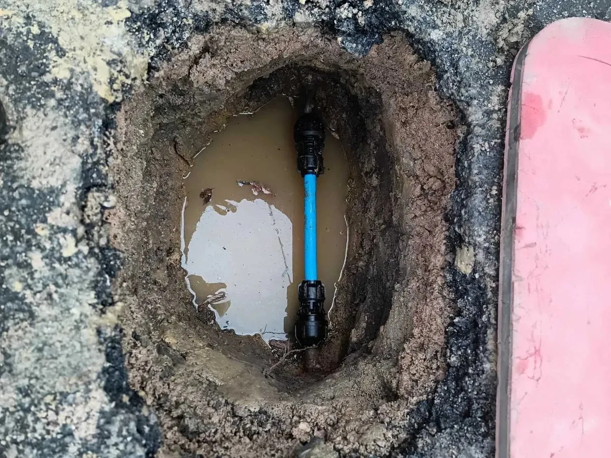 New blue MDPE pipe section with black fittings in the dug-out hole in the tarmac