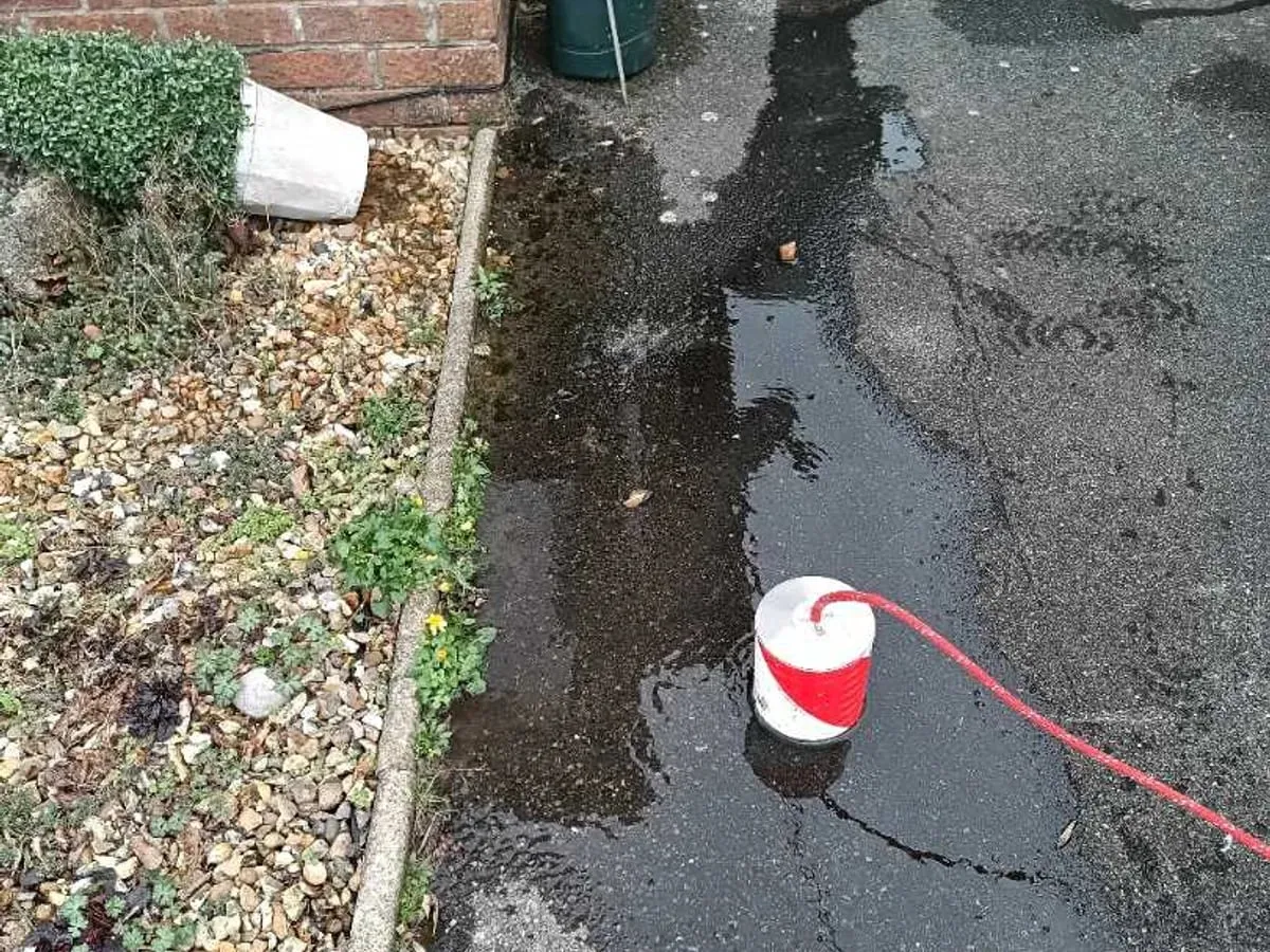 Water running across tarmac beside a gravel border, with a ground microphone placed on the wet patch