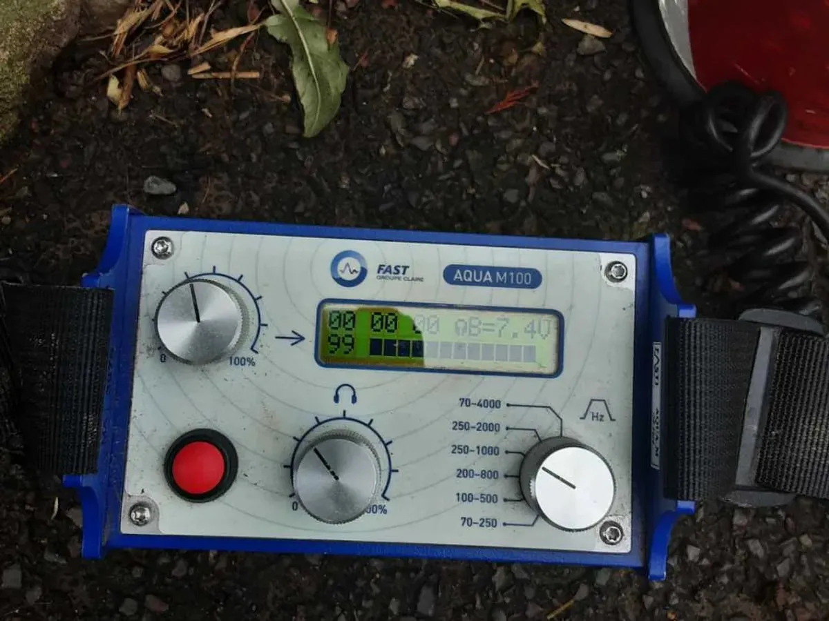 Close-up of a blue acoustic amplifier with a lit display and signal bar, resting on the ground