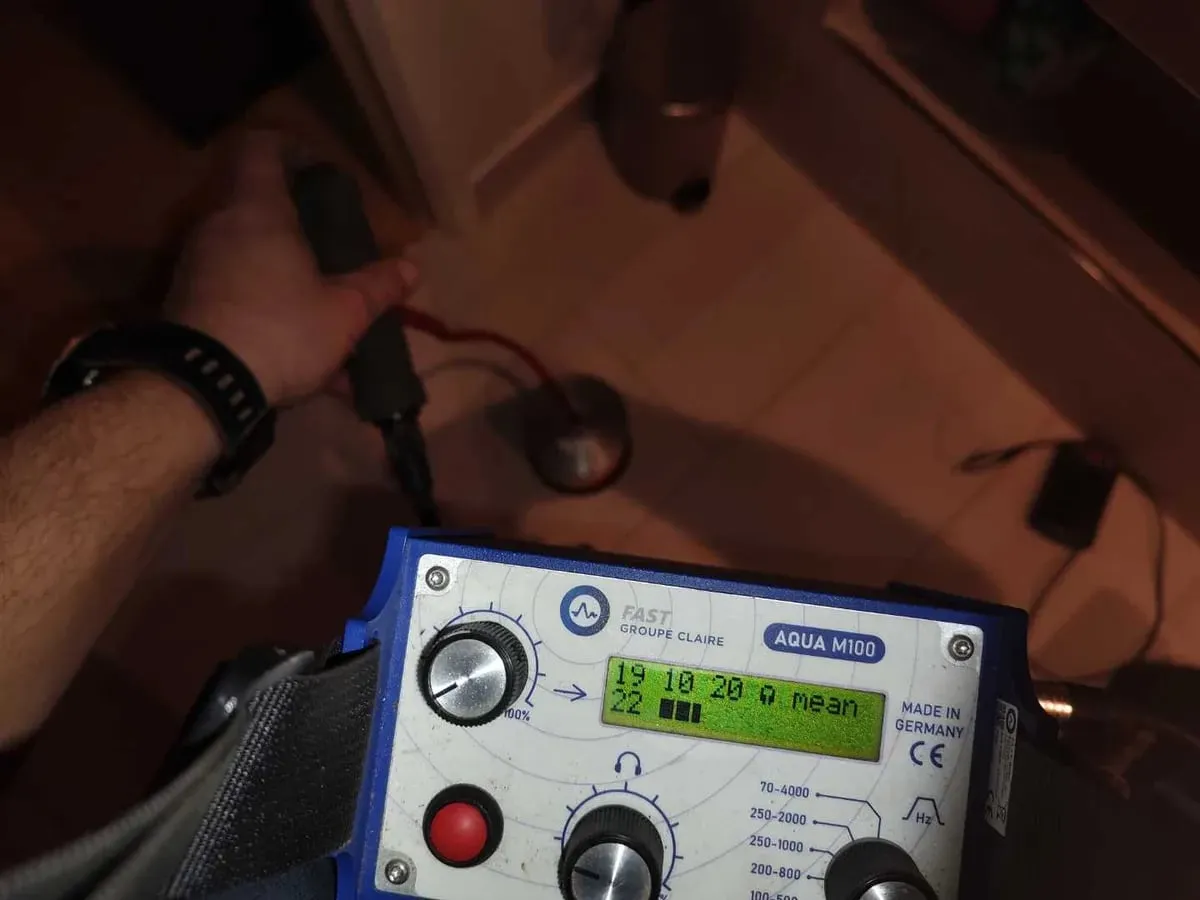 Engineer holding a blue acoustic amplifier with a lit display while listening in a dim corridor