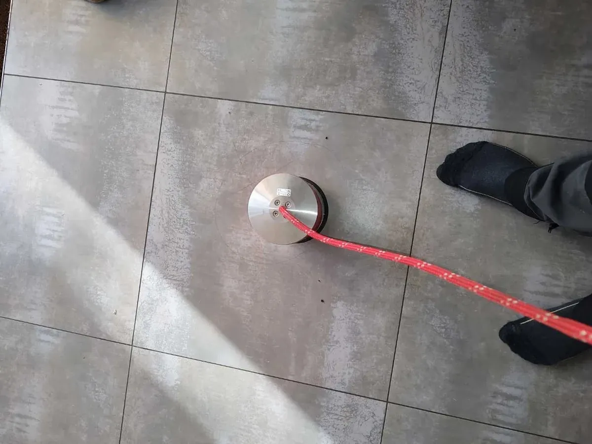 Flat silver ground microphone with a red cable resting on large grey floor tiles